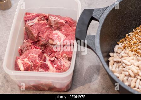 Nahaufnahme des traditionellen jüdischen Cholent Hamin - Hauptgericht für die Schabbat Mahlzeit langsam gekochtes Rindfleisch mit Kartoffeln, Bohnen, Weizenkörnern und Gewürzen in einem Topf auf einem grauen Marmor Küchentisch. Stockfoto