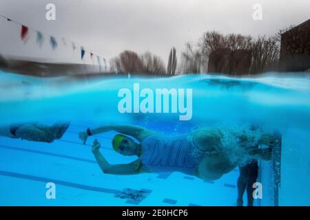 Ein Schwimmer am frühen Morgen dreht sich im Wasser bei Null-Grad-Temperaturen in Charlton Lido im Hornfair Park, London. Stockfoto