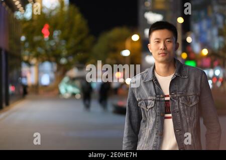 Mittelaufnahme eines asiatischen jungen Mannes in der modernen Stadt bei Nacht, Blick auf die Kamera Stockfoto