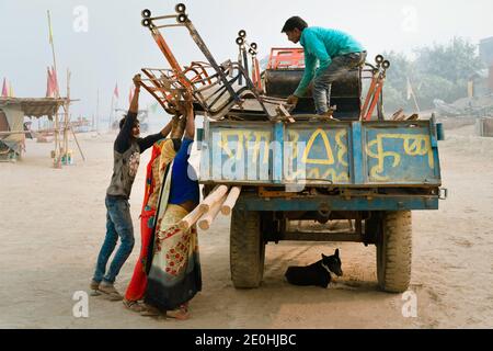 Zwei Omen und ein Mann laden am heißen Sommertag am Fluss Yamuna in Vrindavan, Uttar Pradesh, Indien, demontierte Stühle mit großem Rad auf einen wartenden Lastwagen. Stockfoto