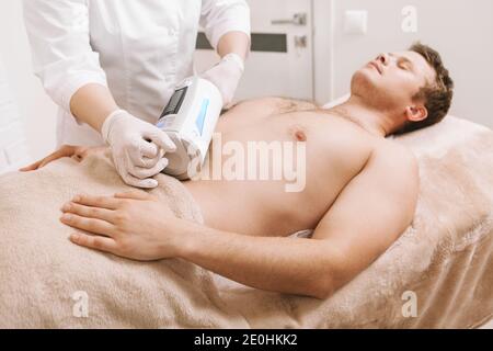 Männliche Klient entspannend, während professionelle Therapeut mit Endospheres Massagegerät Auf dem Bauch Stockfoto