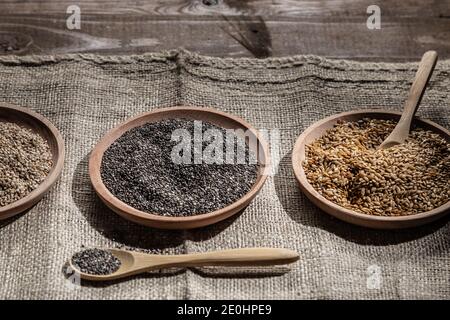 Sesam, Chia und Leinsamen in Holzschalen, Holzlöffel mit Chia auf Holzsockel. Stockfoto