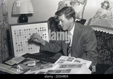 1948, historisch, ein gut gekleideter junger Mann in einer Jacke und Krawatte, der auf einem Sofastuhl sitzt, in einem Raum, der seine Münzsammlung durchläuft, USA. Neben ihm eine große Tafel mit einigen kleinen Münzen mit dem Titel "Lincoln Head Cent", eine Serie von Münzen, die den Kopf des damaligen amerikanischen Präsidenten Abraham Lincoln darstellen. Der Lincoln Cent ist eine ein-Cent-Münze, die die US-Münzstätte seit 1909 produziert, dem Jahr, das Lincolns 100. Geburtstag gewesen wäre. Die von Victor David Brenner entworfenen Münzen sind seitdem beliebte Sammlerstücke. Stockfoto