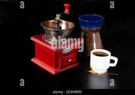 Zutaten für die Herstellung von Kaffee, Vintage Kaffeemühle mit einer Dose Kaffee und eine Tasse auf schwarzem Hintergrund Stockfoto