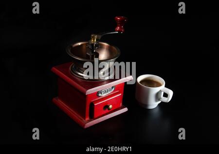 Handgemachte Kaffeemühle mit einer Tasse Kaffee auf schwarzem Hintergrund. Vintage Stockfoto