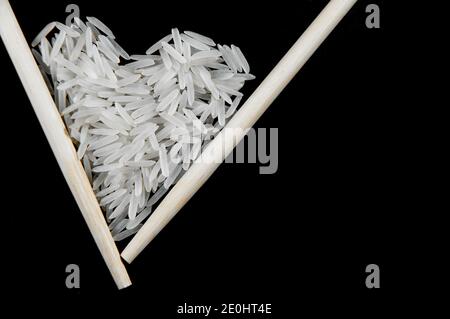 Weißer Reis mit chinesischen Sticks auf schwarzem Hintergrund in Die Form eines Herzens Stockfoto