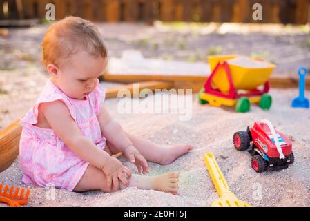 Baby Mädchen spielen in Sandbox auf Spielplatz im Freien. Kind mit bunten Sandspielzeug. Gesundes aktives Baby im Freien spielt Spiele Stockfoto