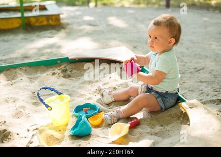 Baby Mädchen spielen in Sandbox auf Spielplatz im Freien. Kind mit bunten Sandspielzeug. Gesundes aktives Baby im Freien spielt Spiele Stockfoto