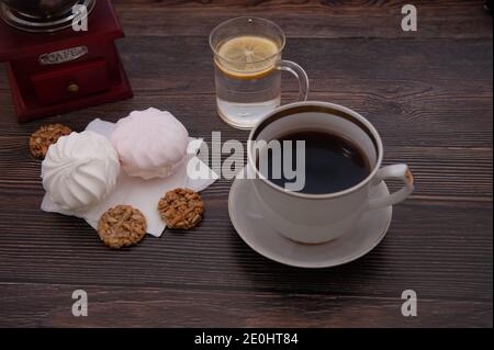 Kaffeekomposition mit Kaffeemühle, Tasse Kaffee, Kekse und Marshmallows vor dem Hintergrund eines dunklen Baumes Stockfoto