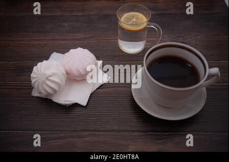 Eine Tasse Kaffee, Wasser mit Zitrone und Marshmallows gegen einen dunklen Baum Stockfoto