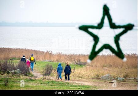 Dangast, Deutschland. Januar 2021. Wanderer sind am Neujahrstag bei bewölktem Wetter am Strand von Dangast, während ein grüner Stern an einer Straßenlaterne im Vordergrund hängt. Quelle: Hauke-Christian Dittrich/dpa/Alamy Live News Stockfoto