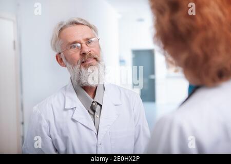 Glücklicher leitender Arzt lächelnd, im Gespräch mit einer Kollegin in der Klinikhalle Stockfoto