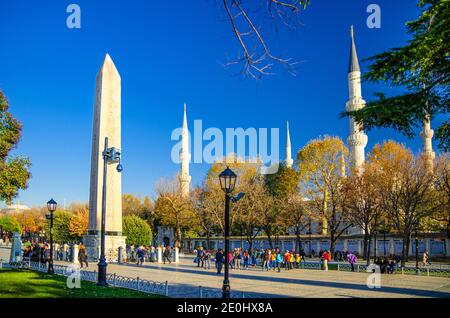 Istanbul, Türkei, 25. November 2017: Sultan Ahmed Moschee Blaue Moschee mit Minaretten, Obelisk von Theodosius Dikilitas und Touristen, die die Fußgängerzone im historischen Stadtzentrum entlang gehen, blauer Himmel Stockfoto