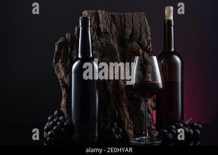 Flaschen, Glas spanischen Rotwein und Trauben auf Holzsockel auf schwarzem und rotem Hintergrund. Stockfoto