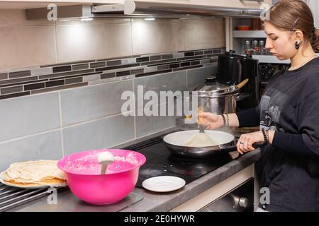 Das Mädchen prüft, ob der Pfannkuchen bereit ist, umgedreht zu werden. Leckere hausgemachte Pfannkuchen aus der Hand einer jungen Frau. Stockfoto