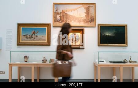 Allein weiße junge Frau, die in einer Kunstgalerie an Ölgemälden vorbeigeht, ist verschwommen und zeigt Bewegungen, während sie ihren Kopf dreht, um die Kunstwerke anzusehen Stockfoto