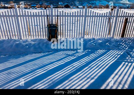 Weißer Vinyl-Pfostenzaun wirft lange Winterschatten auf Neuschnee; Salida; Colorado; USA Stockfoto