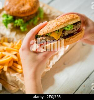 Hände und leckere Burger mit Fleisch, pommes frites, Sauce auf dem Holztisch Stockfoto