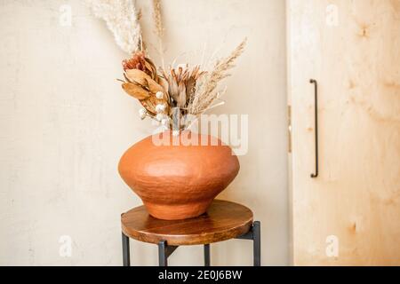 Komposition aus getrockneten Blumen in einer Tonvase auf einem beigen Wandhintergrund. Bouquet von Pampas Gras, cortaderia, Banksia, proteaceae, Gomphrena Stockfoto