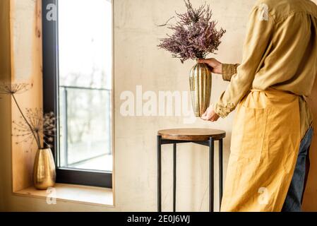 Frau Dekoration Haus mit einer getrockneten Calluna Blume in einem Goldene Vase auf beigefarbenem Wandhintergrund Stockfoto