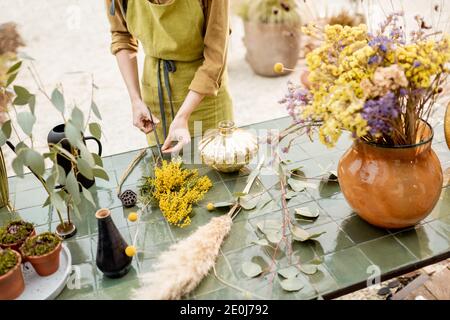 Weibliche Kompositionen aus getrockneten und frischen Blumen und Kräutern auf dem grünen Tisch im Freien. Floristen, Gärtner oder Dekorateur komponieren florale Dekoration Konzept. Nahaufnahme Stockfoto