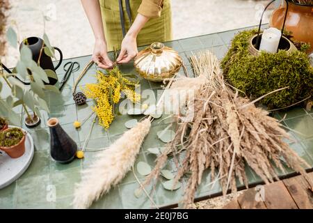 Weibliche Kompositionen aus getrockneten und frischen Blumen und Kräutern auf dem grünen Tisch im Freien. Floristen, Gärtner oder Dekorateur komponieren florale Dekoration Konzept. Nahaufnahme Stockfoto