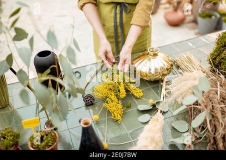 Weibliche Kompositionen aus getrockneten und frischen Blumen und Kräutern auf dem grünen Tisch im Freien. Floristen, Gärtner oder Dekorateur komponieren florale Dekoration Konzept. Nahaufnahme Stockfoto