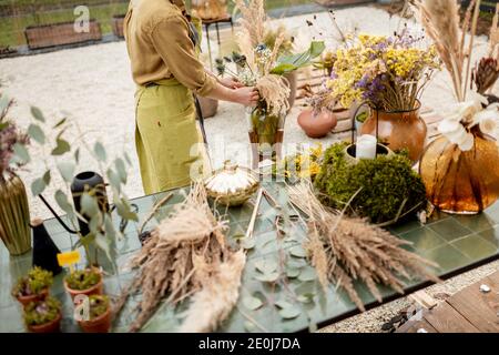 Weibliche Kompositionen aus getrockneten und frischen Blumen und Kräutern auf dem grünen Tisch im Freien. Floristen, Gärtner oder Dekorateur komponieren florale Dekoration Konzept. Nahaufnahme Stockfoto