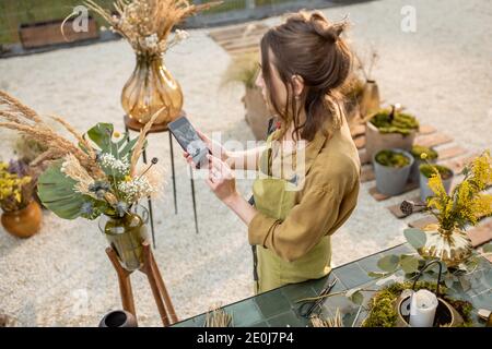 Frau fotografiert auf einem Smartphone Kompositionen von Blumen und Kräutern Während einer Blumenwerkstatt im Freien Stockfoto