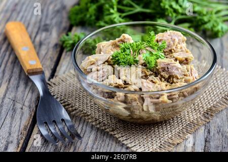 Portion Thunfischsalat mit frischer Petersilie, Kirschtomate und zwei Gabeln auf rustikalem Holztisch. Selektiver Fokus. Stockfoto