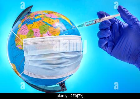 Eine Hand eines Arztes in einem Handschuh injiziert eine Spritze mit dem Coronavirus-Impfstoff in einen Erdball, der mit einer chirurgischen Gesichtsmaske bedeckt ist. Konzept der Welt Stockfoto
