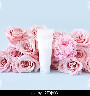 Mockup von nicht gebrandeten weißen Flasche für Branding und Label und hellrosa Rosen auf einem pastellblauen Hintergrund. Flasche Plastikschlauch zusammendrücken. Natürlich organisch Stockfoto