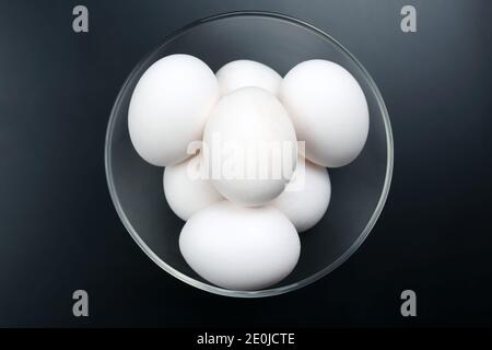 Weiße Hühnereier liegen auf dem Teller auf einem dunklen Hintergrund Stockfoto