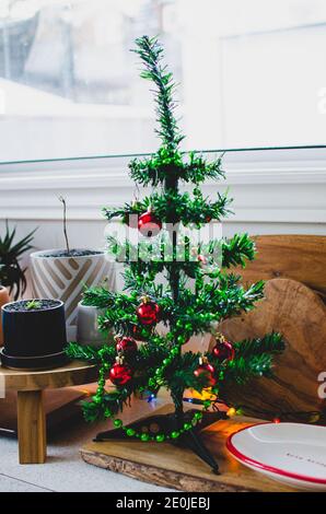 Leuchtend rote Kugeln leuchten auf einem Miniatur-Weihnachtsbaum In der Küche Stockfoto