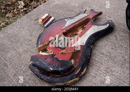 Die Stücke einer gebrochenen roten Gitarre liegen zusammen auf rauem Beton. Stockfoto