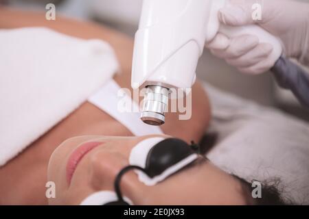 Beschnitten Nahaufnahme einer Kosmetikerin tun Gesichtshaar Laser-Entfernungsverfahren auf eine weibliche Client. Frau bekommen Laser Hautpflege Behandlung in der Beauty-Klinik Stockfoto