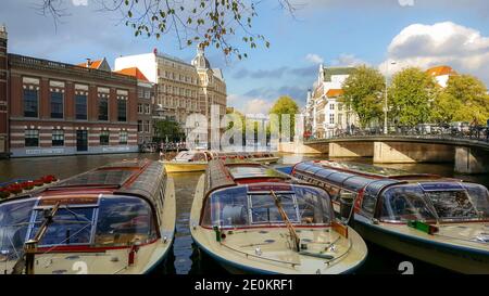 Bunte gelbe und rote Ausflugsboote warten auf Touristen Passagiere auf einem großen Kanal in Amsterdam, Niederlande Stockfoto