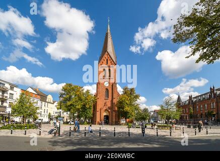 Der neugotische Kirchturm der Warnemunde erhebt sich über der Küstenstadt Warnemunde Rostock, Deutschland, während Touristen und Einheimische einen schönen Sommertag genießen. Stockfoto