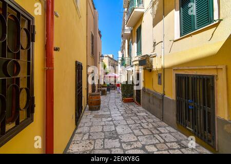 Eine Frau läuft eine bunte enge Gasse hinunter in Richtung eines Cafés in der italienischen Stadt Brindisi Italien, in der Region Apulien. Stockfoto