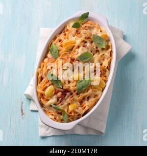 Gebackene Pasta mit Tomatensauce, Knoblauch, Käse und Basilikum in weißer Keramikform auf hellblauem Hintergrund. Leckeres hausgemachtes Essen Stockfoto