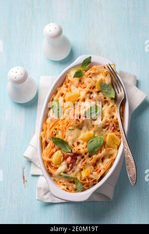 Gebackene Pasta mit Tomatensauce, Knoblauch, Käse und Basilikum in weißer Keramikform auf hellblauem Hintergrund. Leckeres hausgemachtes Essen Stockfoto