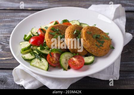 Karottenschnitzel mit Amaranth, Salat mit frischen Gurken und Tomaten auf einem Holztisch. Köstliche gesunde hausgemachte Speisen Stockfoto