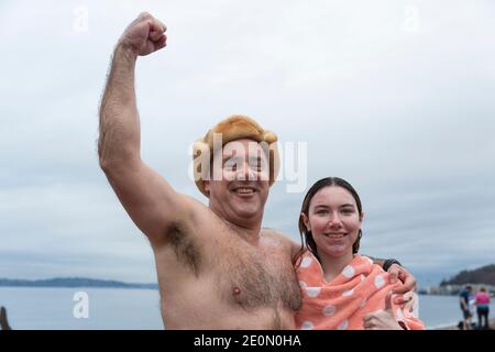 Seattle, Washington, USA. Januar 2021. Brian Callanan in einem warmen Hut mit Tochter Emma Pose für ein Foto nach dem Eintauchen beim jährlichen West Seattle Eisbären Schwimmen im Alki Beach Park. Die Organisatoren arrangierten physisch distanzierte Orte und gestaffelte Timing entlang Alki Beach für die Teilnehmer inmitten einer kürzlichen Moderation von COVID-19 Fällen in der Stadt. Quelle: Paul Christian Gordon/Alamy Live News Stockfoto