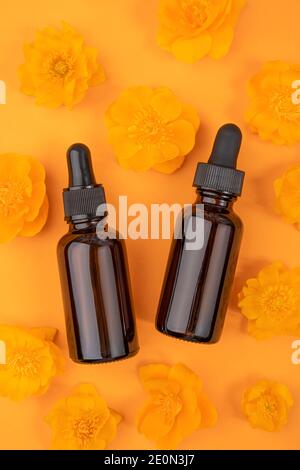Zwei braune Glasflaschen mit Serum, ätherischem Öl oder anderen kosmetischen Mitteln und orangen Blüten auf orangefarbenem Hintergrund. Natürliches Organisches Spa Kosmetisches Beau Stockfoto