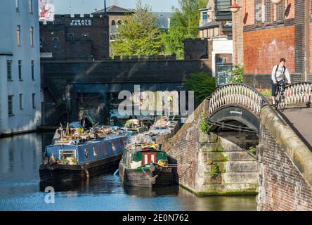 Ein Radfahrer passiert eine kleine Brücke auf dem Abflutweg des Regent's Canal bei Camden Lock, London, England. Hinter ist das Piratenschloss, ein Boot und Stockfoto