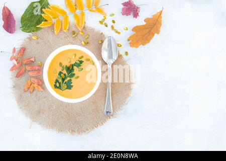 Kürbis- und Karottensuppe mit Kürbiskernen und Petersilie auf weißem Hintergrund mit Herbstblättern. Draufsicht. Speicherplatz kopieren Stockfoto