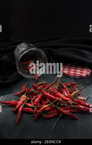 Nahaufnahme von einem Bündel roter Chilischoten auf einem rustikalen Holztisch. Ein verschwommenes transparentes Glas hat einige zusätzliche Paprika im Inneren neben seinem m Stockfoto