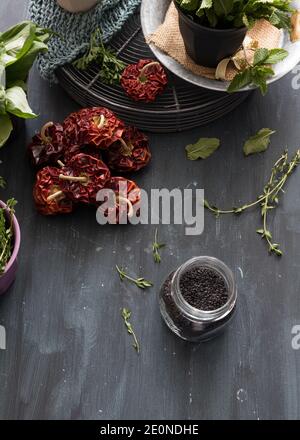 Glas voller schwarzer Sesamsamen im unteren Teil eines Stilllebens, bestehend aus aromatischen Pflanzentöpfen und roten Paprika. Stockfoto