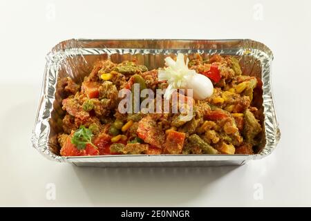 Gemüse in Metallfolie mit rohem Gemüse auf weißem Hintergrund mischen. Stockfoto