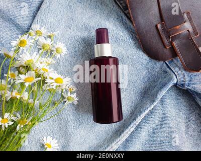 Draufsicht auf dunkelbraune Sprühflasche Mock-up und Kamillen auf einem blauen Jeans Hintergrund. Leere Etikettenflasche zum Branding. Natürliche Bio-Spa-Kosmetik c Stockfoto